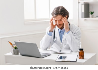 Professional burnout. Tired male doctor suffering from headache at workplace, free space
