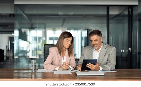 Professional business executives office team working using digital tablet computer sitting at table. Two middle aged colleagues company board discussing smart technology at corporate meeting. - Powered by Shutterstock