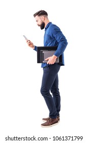 Professional business male executive checking phone carrying tablet and laptop under arm. Side view. Full body isolated on white background.