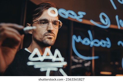 Professional business man brainstorming on a glass wall in an office, working late to meet his deadline. Data analyst engaging in strategising and creative thinking for a business project. - Powered by Shutterstock