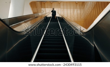 Professional business man using phone calling while using escalator. Skilled caucasian executive manager talking to business team to report and discuss marketing idea or plan. Front view. Exultant.