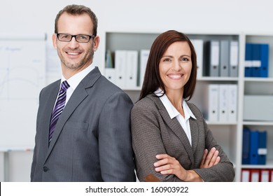 Professional Business Man And Woman Standing Back To Back In The Office Looking At The Camera With Confident Smiles At The Success Of Their Partnership