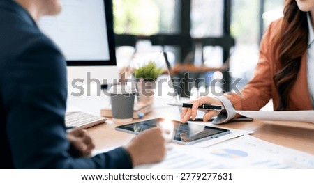 Professional business team analyzing data on a digital tablet and paper reports during a meeting in a bright modern office.