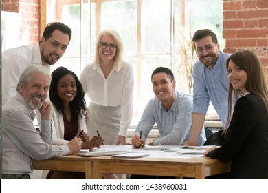 Professional business team young and old people posing together at office table, happy diverse leaders employees looking at camera, smiling multiracial staff corporate people workers group portrait