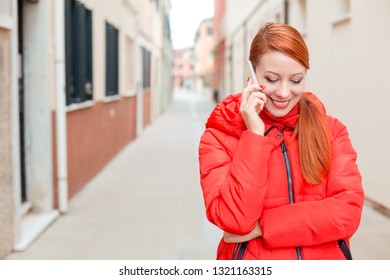 Professional Business Woman On Smartphone Smiling Happy Wearing Red Coat Outwear. Young Happy Casual Woman Talking On Smart Phone Walking Outdoor In Fall Or Winter On A Italian Street. Caucasian Model