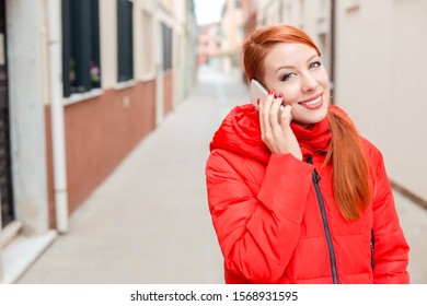 Professional Business Woman On Smartphone Smiling Happy Wearing Red Coat Outwear. Young Happy Casual Woman Talking On Smart Phone Walking Outdoor In Fall Or Winter On A Italian Street. Caucasian Model