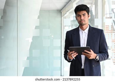 Professional businessman in black suit holding digital tablet and looking confidently at camera.