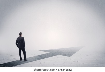 A professional businessman thinking while standing on a black arrow pointing forward in grey space concept - Powered by Shutterstock