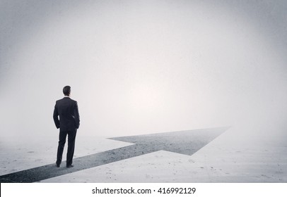 A professional businessman thinking while standing on a black arrow pointing forward in grey space concept - Powered by Shutterstock