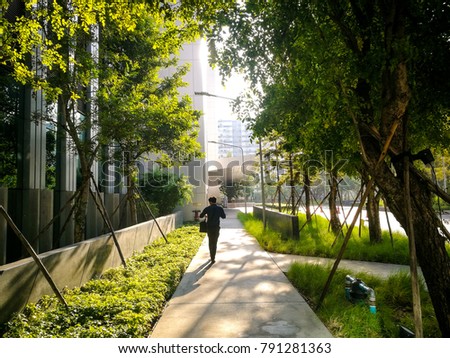 Professional businessman walking near small garden and big modern office in the morning with rays sunlight. working life in the city with green environment.