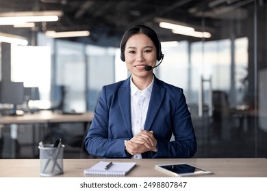 Professional businesswoman in formal attire communicating through a video call in a modern office environment. She is looking at the camera and wearing a headset, conveying professionalism - Powered by Shutterstock