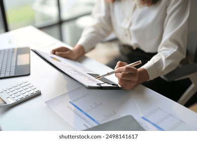 Professional businesswoman reviewing financial charts and graphs on a clipboard at a modern office desk. - Powered by Shutterstock