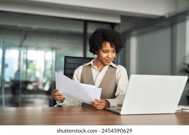 Professional busy young African American business woman account manager executive checking document financial report using laptop checking file working with enterprise software sitting at office desk. - Powered by Shutterstock