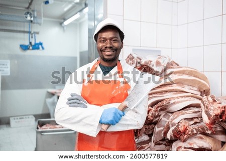 Professional butcher with sharp cleaver working with raw meat in slaughterhouse.