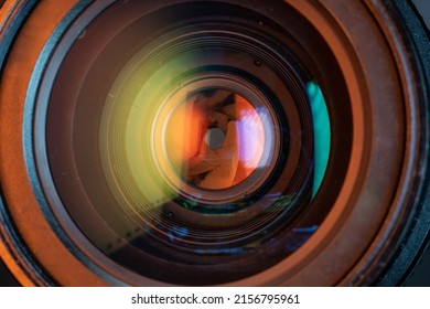Professional camera photo lens. Details of glass, aperture petals. Light reflections from modern diode lamps. The concept of making visual content. Warm, orange colors