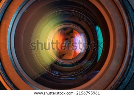 Professional camera photo lens. Details of glass, aperture petals. Light reflections from modern diode lamps. The concept of making visual content. Warm, orange colors