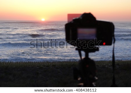 Professional camera set on a tripod with filter to capture video of a sunrise