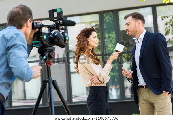 professional cameraman and journalist\
interviewing businessman near office building\

