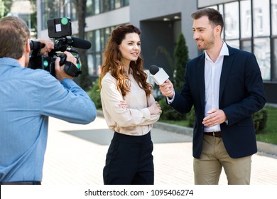 Professional Cameraman And Male News Reporter Interviewing Smiling Businesswoman  