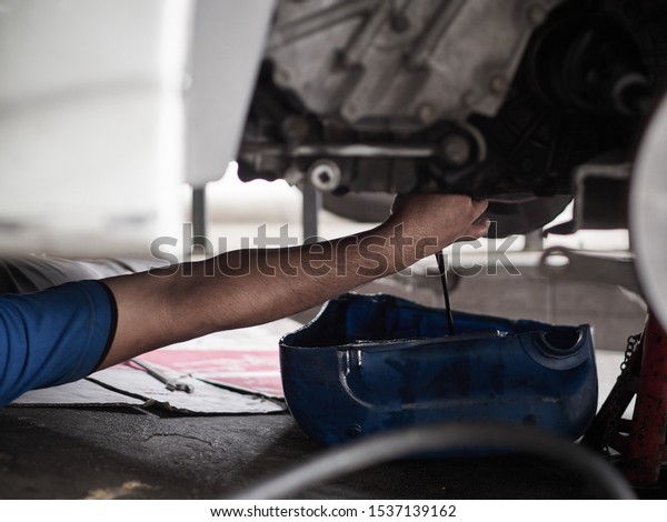 Professional car mechanic changing\
motor oil under car at the garage. Mechanic oil change service.\
