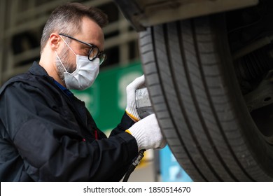 Professional Car Mechanic Changing Car Wheel At Car Maintenance And Auto Service Garage. Caucasian Man Worker People. Surgical Face Mask Protec Coronavirus Covid 19.