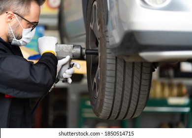 Professional Car Mechanic Changing Car Wheel At Car Maintenance And Auto Service Garage. Caucasian Man Worker People. Surgical Face Mask Protec Coronavirus Covid 19.