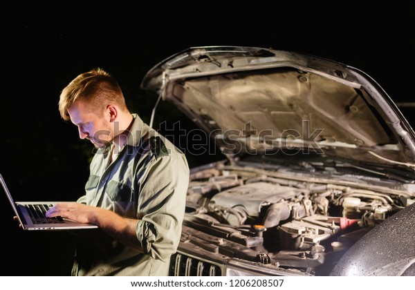 A professional car mechanic standing with
his back to the car, working in a car service, using a laptop to
set up and check maintenance.