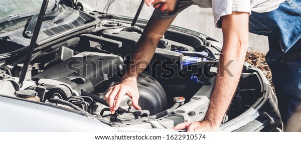 Professional car\
mechanic in uniform  fixing a car engine and repairing checking\
under the car hood in auto service\
