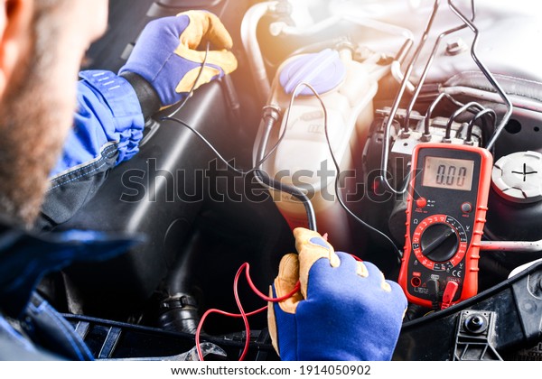 Professional car mechanic use electrician\
voltage multimeter, working in auto repair\
service.