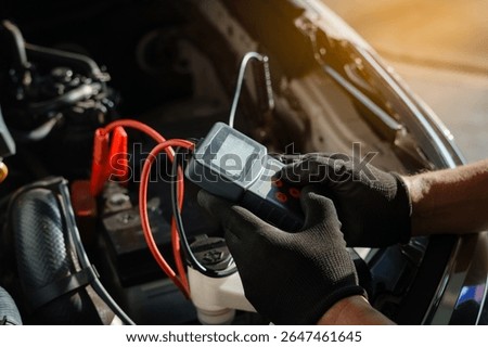 Professional car mechanic using a digital battery tester to inspect vehicle performance during routine maintenance. Automotive technician  performing diagnostics under the hood in a repair shop.