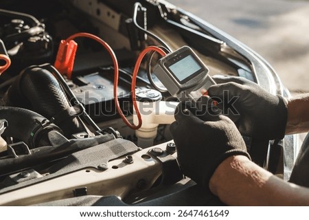 Professional car mechanic using a digital battery tester to inspect vehicle performance during routine maintenance. Automotive technician performing diagnostics under the hood in a repair shop.