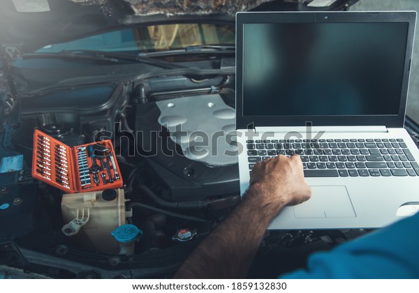 Professional car mechanic working in auto repair\
service using laptop on\
car\
\
