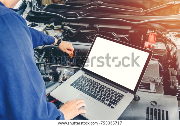 Professional car mechanic working in auto repair\
service using laptop on\
car