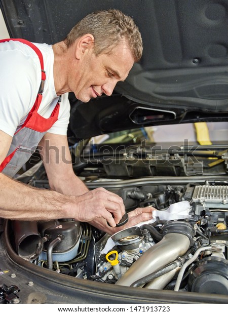 a professional car mechanical of a\
car service workshop stand at the open bonnet motor engine and make\
a oil check and change in the garage of his\
company