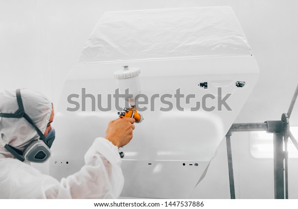 Professional car painter painting door of a car\
with primer.