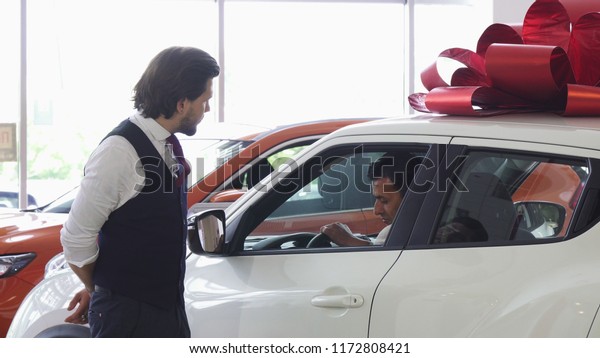 Professional car salesman opening door of a car\
for his male\
customer