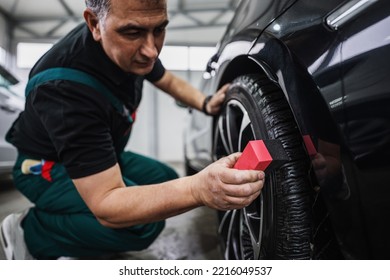 Professional Car Service Worker Polishing Luxury Car Rim With Microfiber Rag Or Cloth In A Car Detailing And Valeting Shop. Ultra Wide Angle Shot.