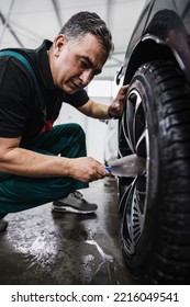 Professional Car Service Worker Polishing Luxury Car Rim With Microfiber Rag Or Cloth In A Car Detailing And Valeting Shop. Ultra Wide Angle Shot.