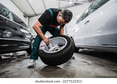 Professional car service worker polishing luxury car rim with microfiber rag or cloth in a car detailing and valeting shop. Ultra wide angle shot.