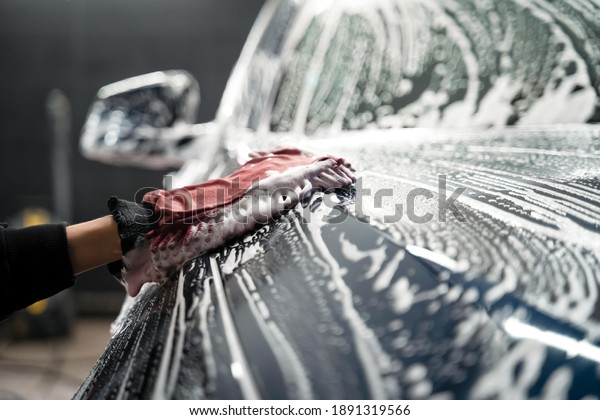 Professional car wash. Detailing worker washes the\
vehicle body with foam and\
rag