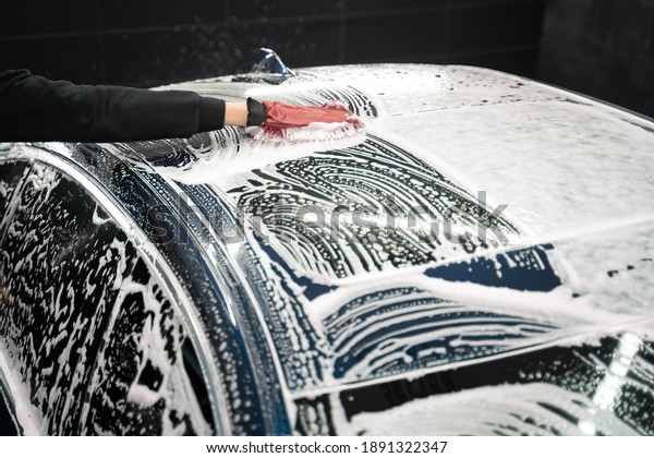 Professional car wash. Detailing worker washes the\
vehicle body with foam and\
rag