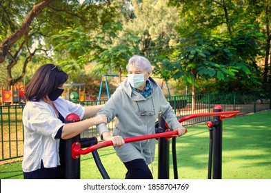 A Professional Caregiver Helps An Elderly Woman To Start Exercise On An Air Walker Fitness Machine. Both Wearing Face Medical Masks Because Of The Coronavirus Pandemic.