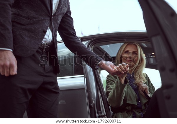 Professional caring hotel\
employee offering a hand supporting a beautiful woman stepping out\
of the taxi