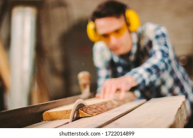 Professional carpenter using sawing machine for cutting wooden board at sawmill. Skilled cabinet maker working with electric circular saw at woodworking workshop. Man joiner, wood production workbench