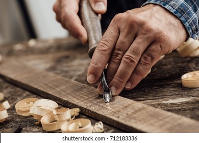 Professional carpenter at work, he is carving wood using a woodworking tool, hands close up, carpentry and craftsmanship concept