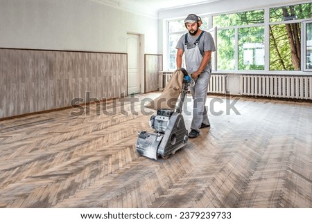 Professional carpenter worker grinding a wooden parquet floor by using floor sander. Industrial theme