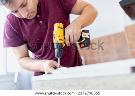 Professional carpenter working with electric cordless screwdriver. Kitchen installation concept.