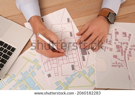 Professional cartographer working with cadastral map at wooden table, top view