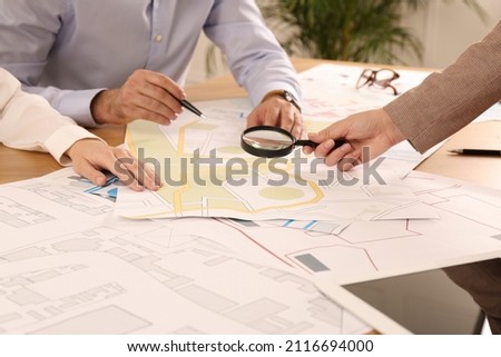 Professional cartographers working with cadastral map at table in office, closeup