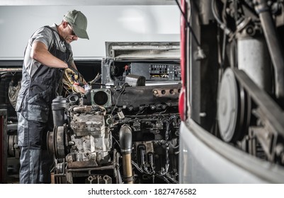 Professional Caucasian Automotive Mechanic In His 40s Repairing Powerful Heavy Duty Truck Or Bus Diesel Engine Inside Truck Service Center. Transportation Industry Theme.